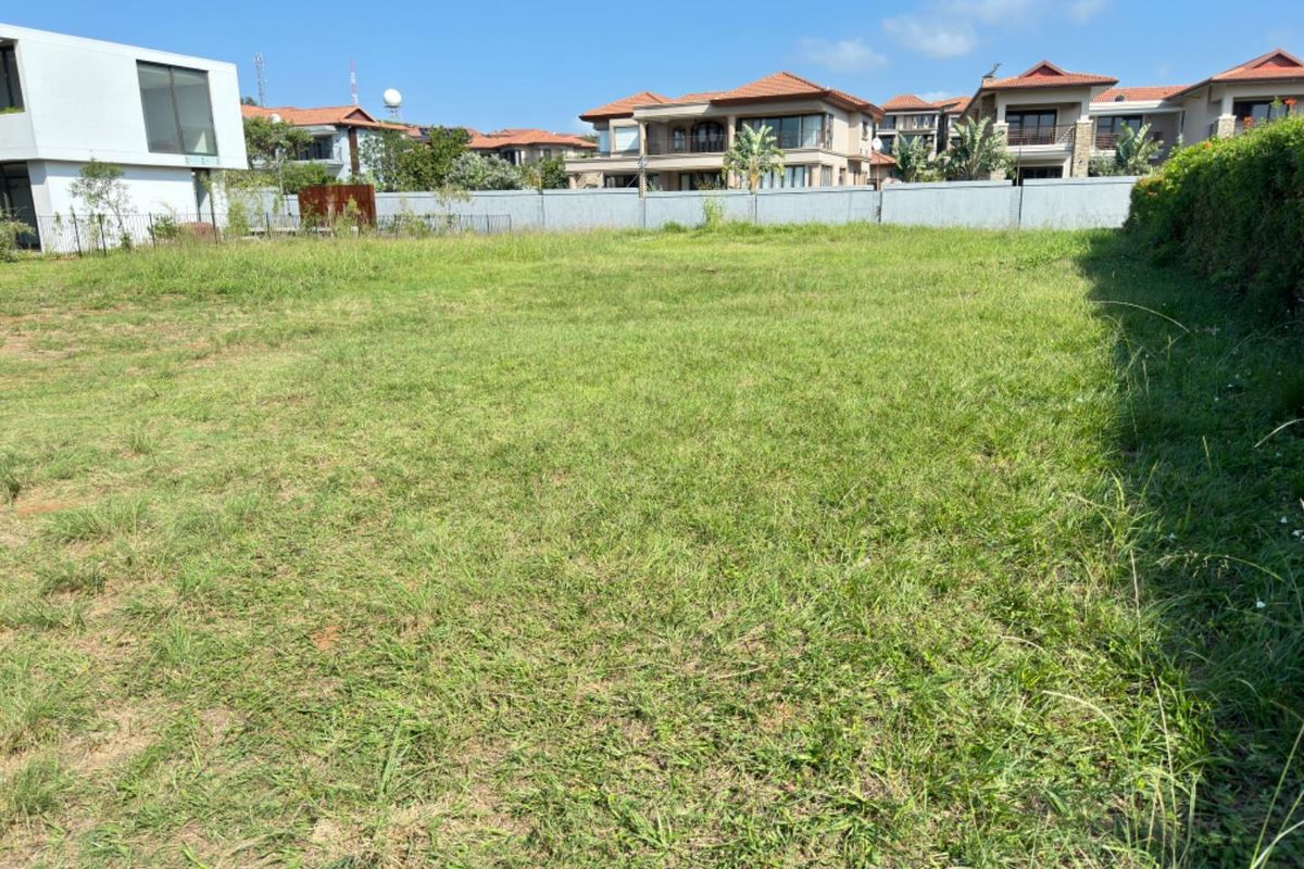A vacant residential plot of land featuring level grass coverage, enclosed by perimeter boundary walls, situated within a developed residential estate.