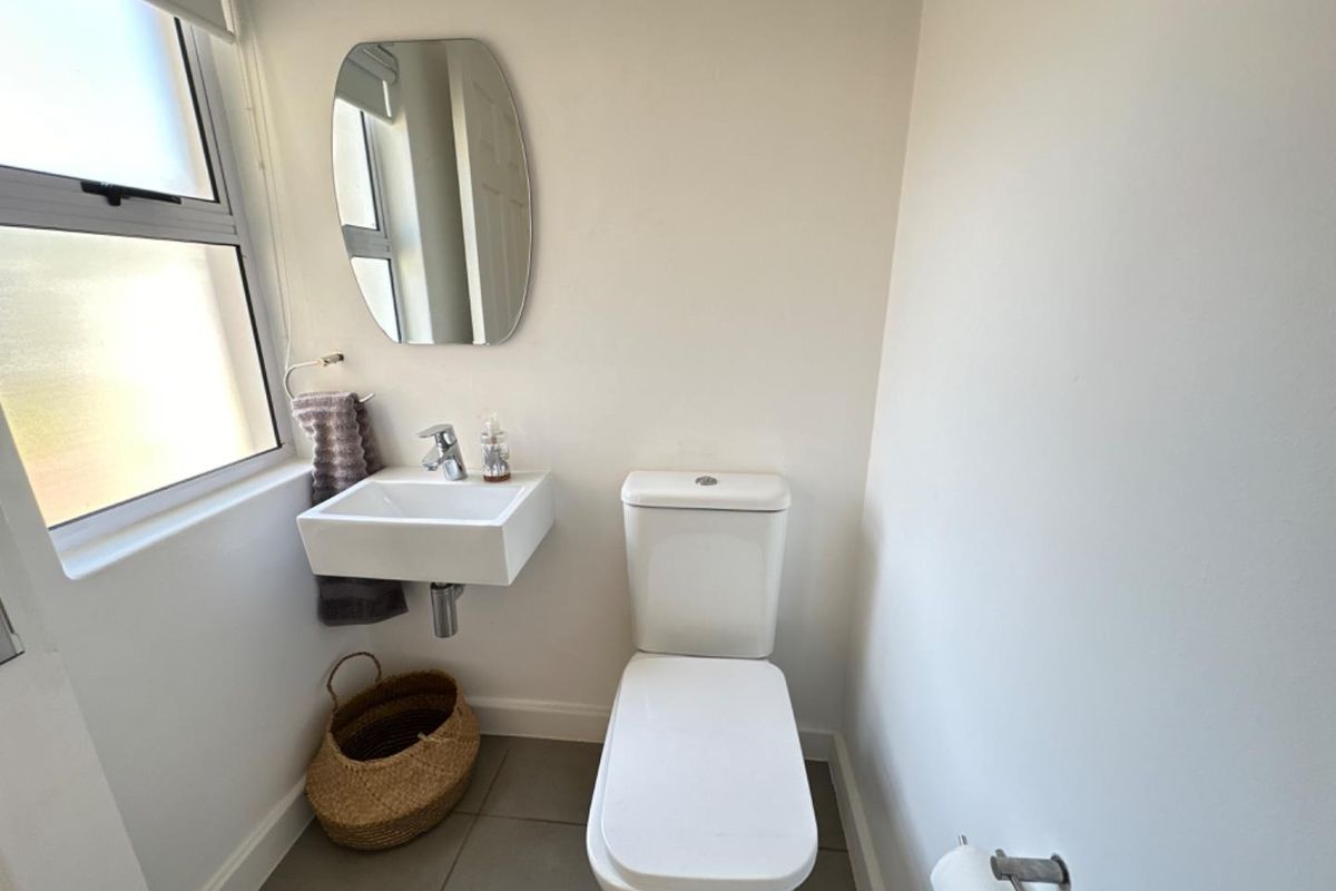 A compact guest bathroom featuring a wall-mounted basin, modern toilet, and tiled flooring, providing a clean and functional space.