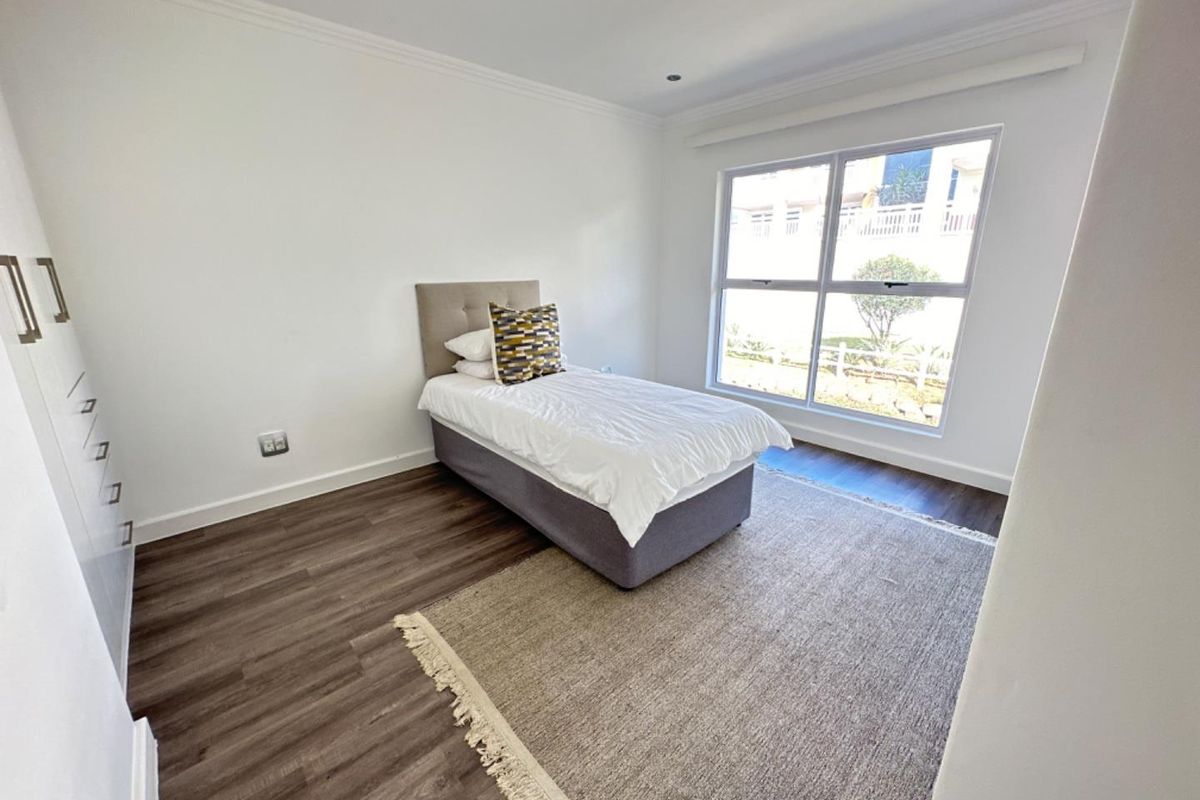 A bright bedroom featuring modern wood-look flooring, built-in cabinetry, and large windows providing natural light.