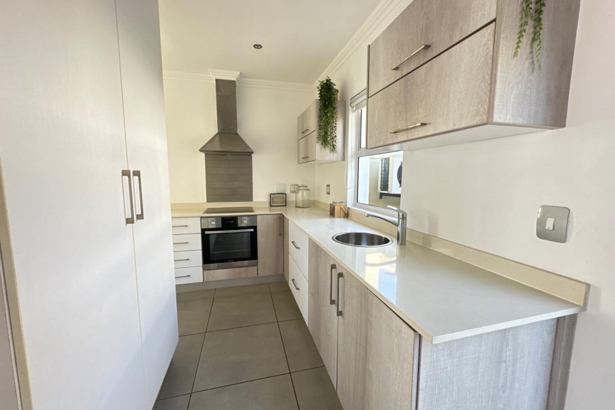 Modern kitchen featuring light wood-grain cabinetry, stone countertops, built-in oven, extractor fan, and tiled flooring.