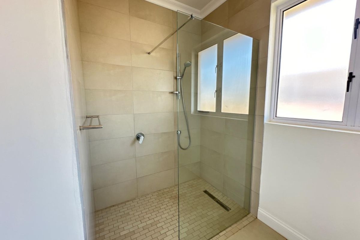 A modern walk-in shower featuring neutral wall tiling, a glass partition, a handheld shower head, and a linear floor drain.