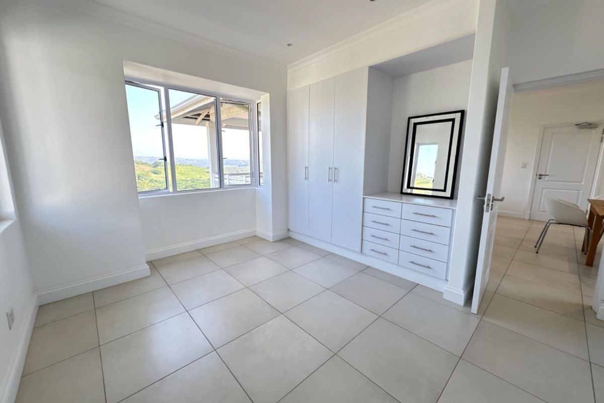 A bright bedroom featuring neutral floor tiles, built-in cabinetry with integrated drawers, and large windows offering scenic views.