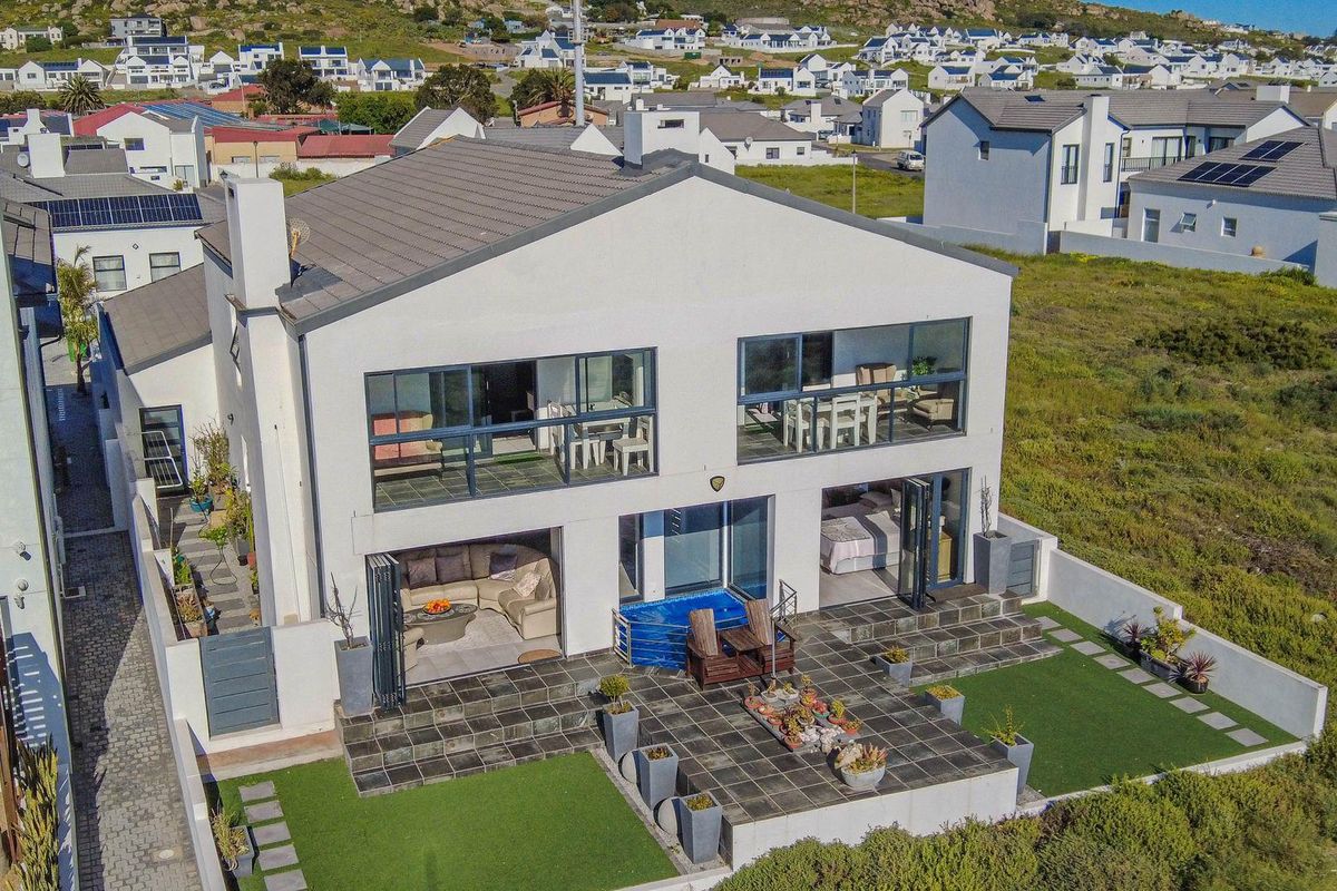 Aerial view of a modern two-story house featuring a tiled patio, artificial lawn, built-in pool, and large glass sliding doors on both levels.