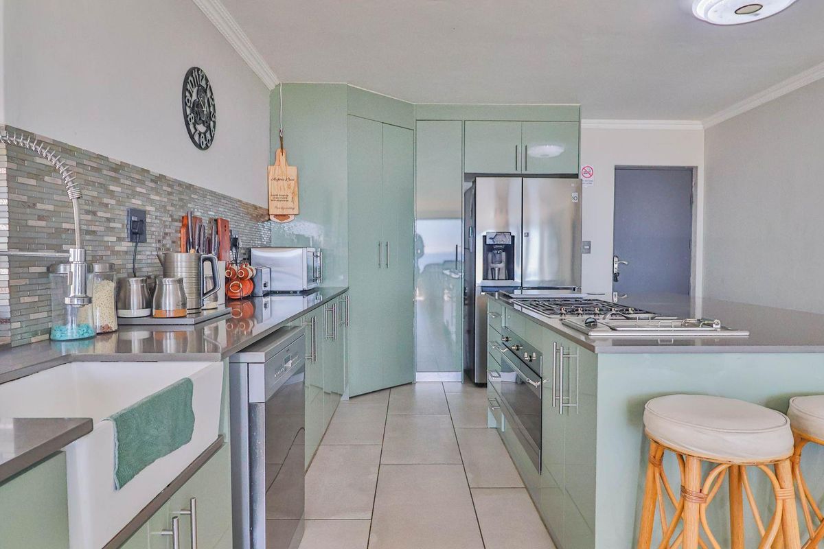 Modern kitchen featuring light green cabinetry, a central island with a built-in gas hob and oven, and a farmhouse-style sink with mosaic tile backsplash.