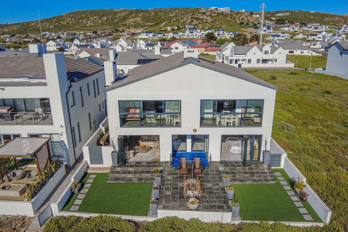 Aerial view of the rear elevation featuring a paved patio, small plunge pool, artificial lawn, and upper-level balconies with sliding glass doors.