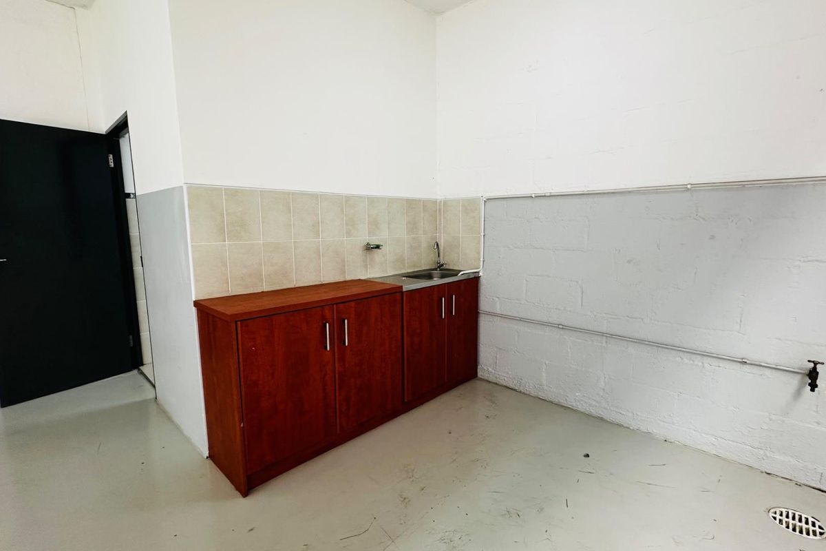 A functional industrial kitchenette area featuring built-in wooden cabinetry, a stainless steel sink, and tiled splashback within a clean, utilitarian workspace.