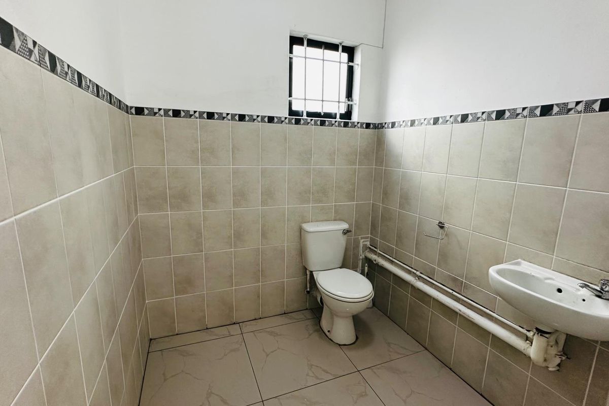 A functional bathroom featuring tiled walls with a decorative border, a standard toilet, and a wall-mounted basin with exposed plumbing.