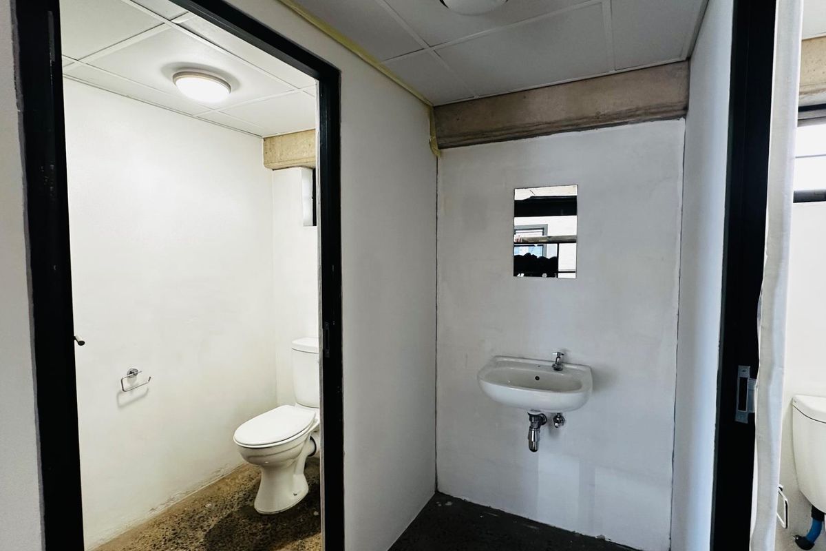 A functional commercial restroom facility featuring a separate toilet cubicle and a wall-mounted basin with basic finishes.