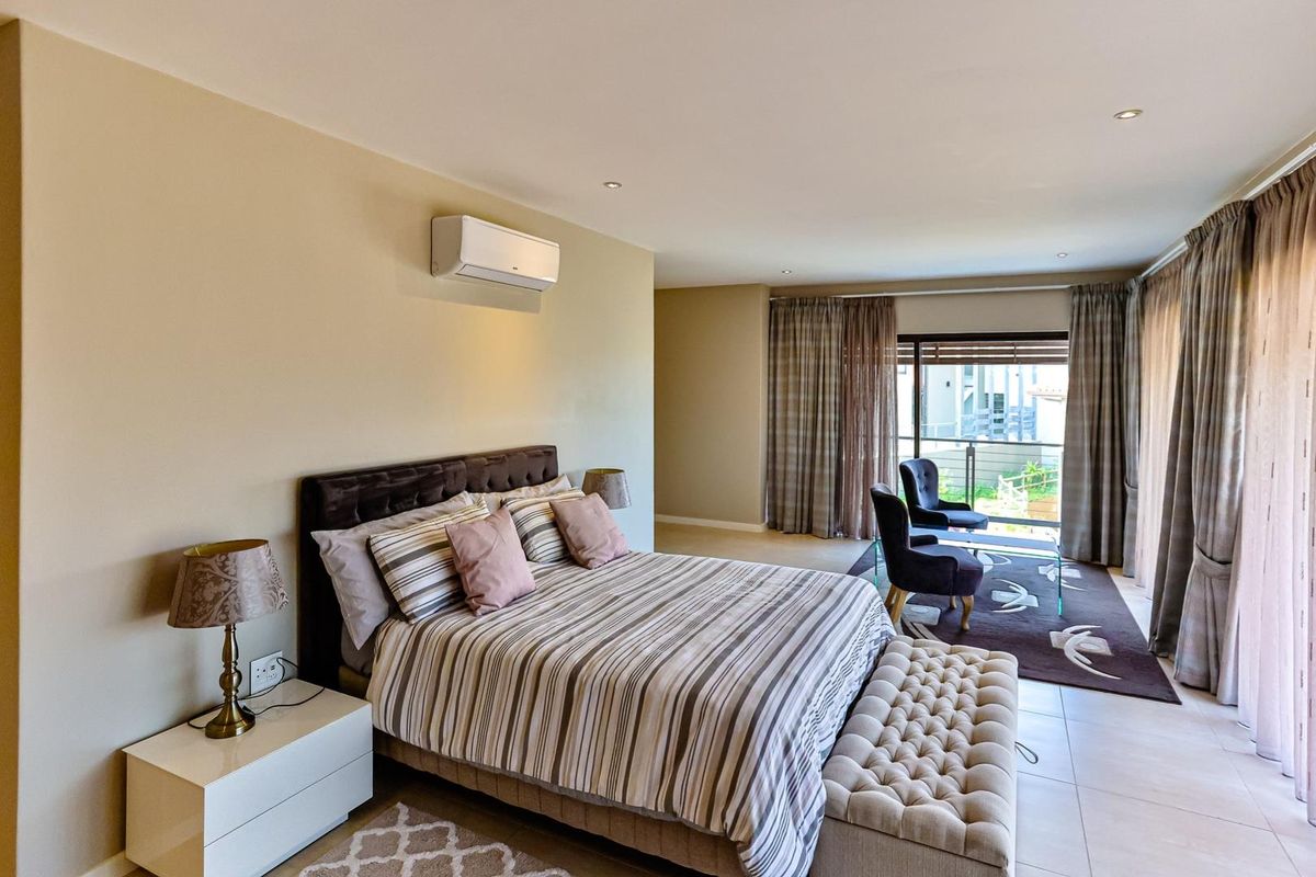 Spacious bedroom featuring neutral tiled flooring, recessed ceiling lighting, and a wall-mounted air conditioning unit, with direct access to a private balcony.