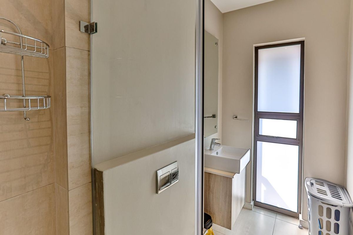 A modern bathroom featuring a glass-enclosed shower, a wall-mounted vanity with a basin, and a frosted glass window for privacy.