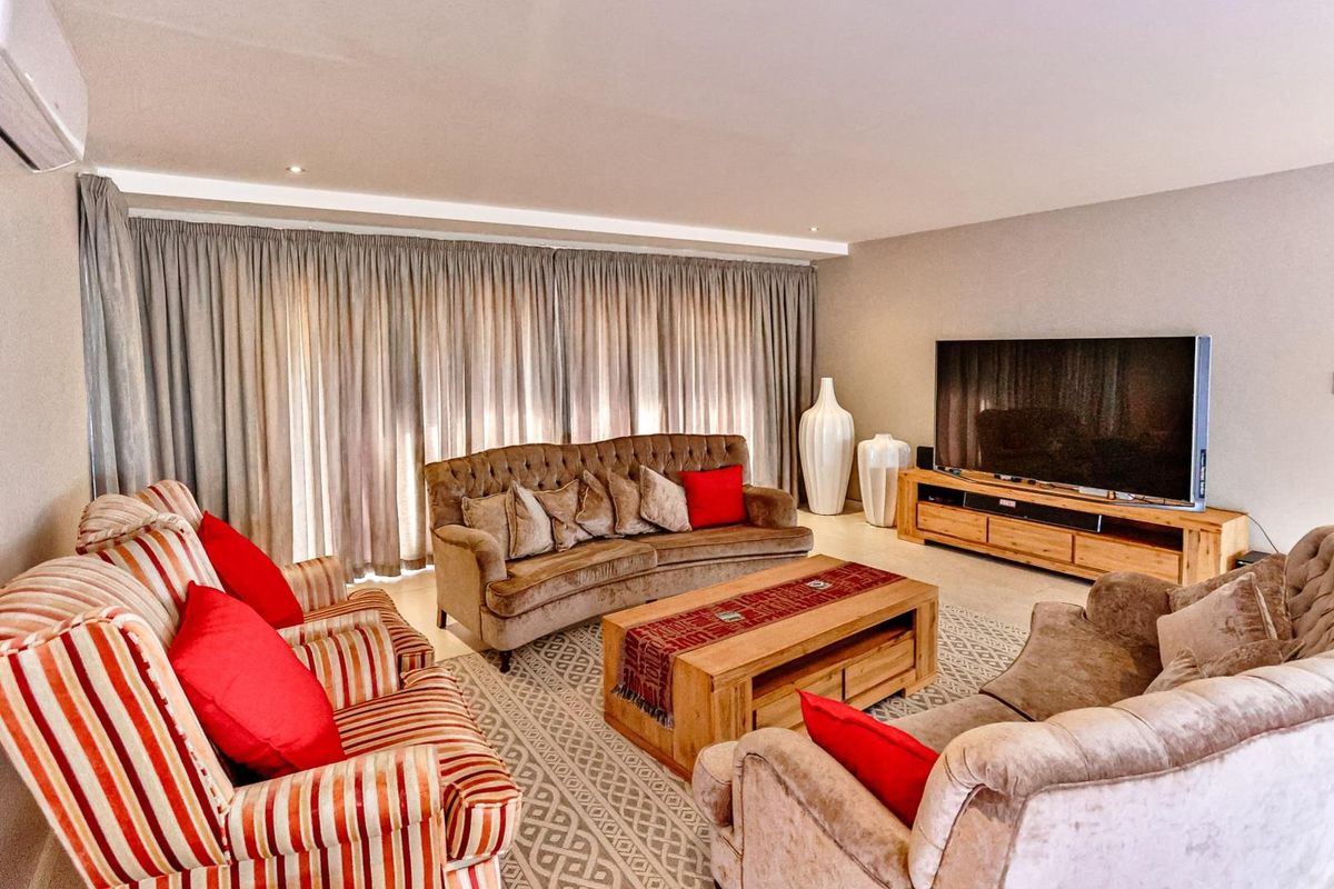A spacious and well-lit living room featuring recessed ceiling lighting, tiled flooring, and large floor-to-ceiling curtains.