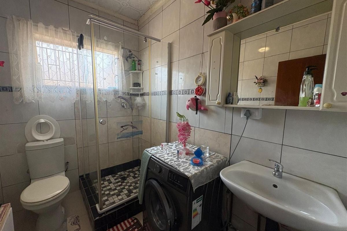 A compact bathroom featuring a glass-enclosed shower, pedestal basin, wall-mounted mirror cabinet, and integrated laundry plumbing connections.