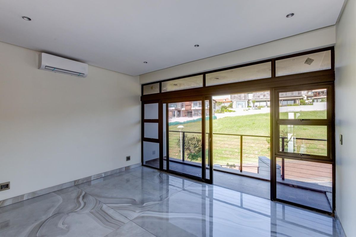 Bright, empty living area featuring polished marble-style floor tiles, recessed ceiling lighting, a wall-mounted air conditioning unit, and large sliding glass doors opening to a balcony.