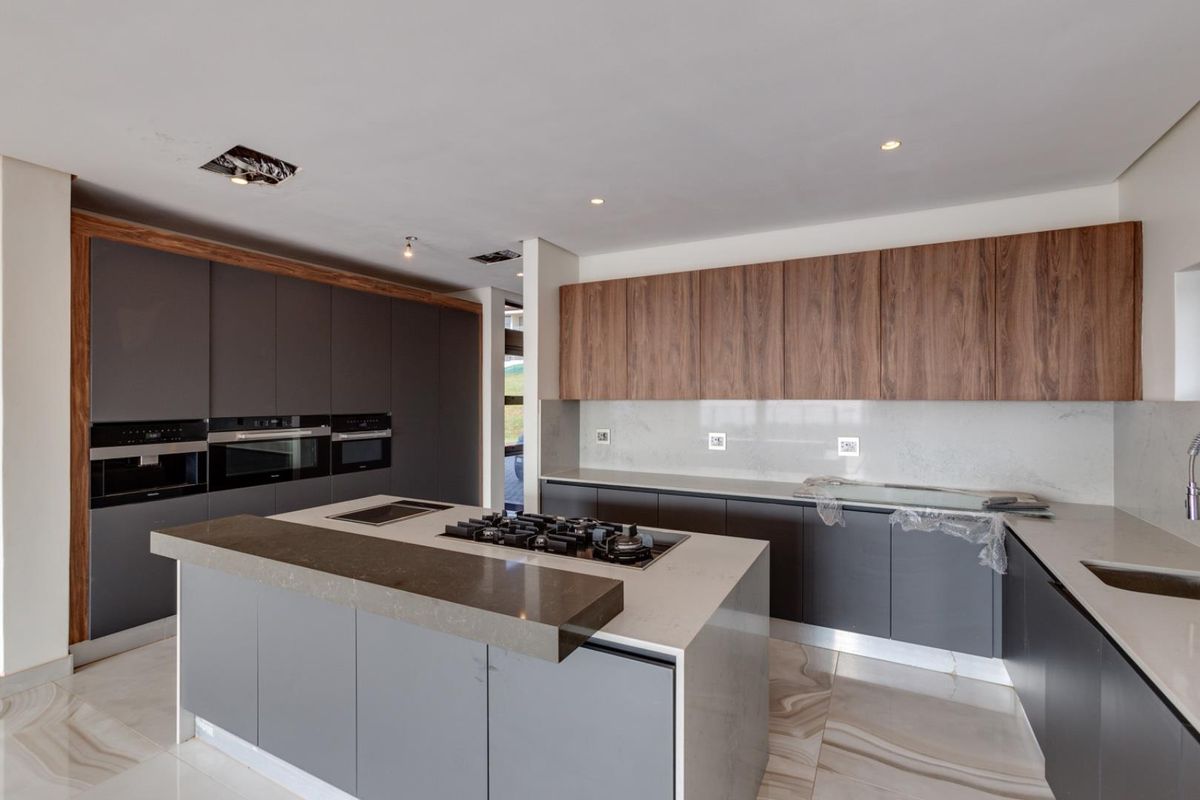 Modern kitchen featuring a large central island with integrated gas hob, sleek dark cabinetry, wood-grain upper cabinets, and stone countertops.
