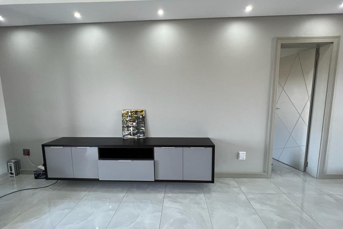 A modern living area featuring polished porcelain floor tiles, recessed ceiling lighting, and a contemporary built-in media console.