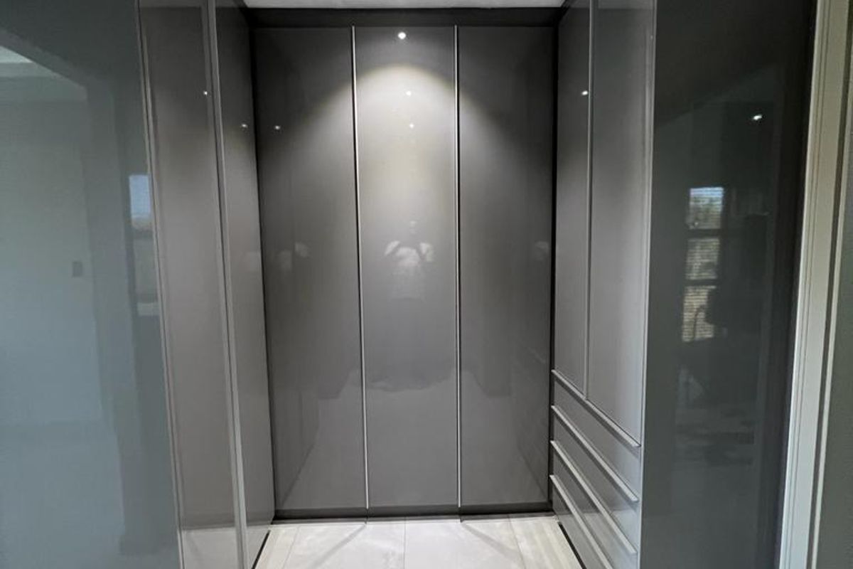 Modern walk-in closet featuring high-gloss grey cabinetry, integrated storage drawers, and polished porcelain floor tiles with recessed downlighting.