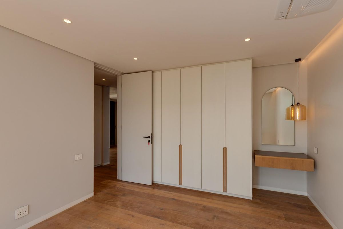 A modern bedroom featuring high-quality timber flooring, built-in floor-to-ceiling cabinetry, recessed ceiling lighting, and a sleek wall-mounted vanity unit.