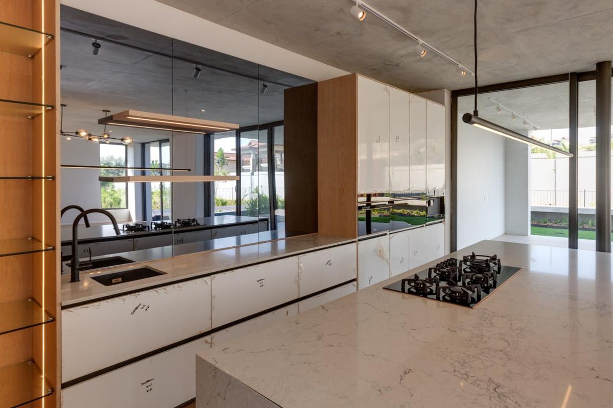 Modern open-plan kitchen featuring a large marble-topped island, integrated gas hob, sleek cabinetry, and a mirrored backsplash with recessed track lighting.