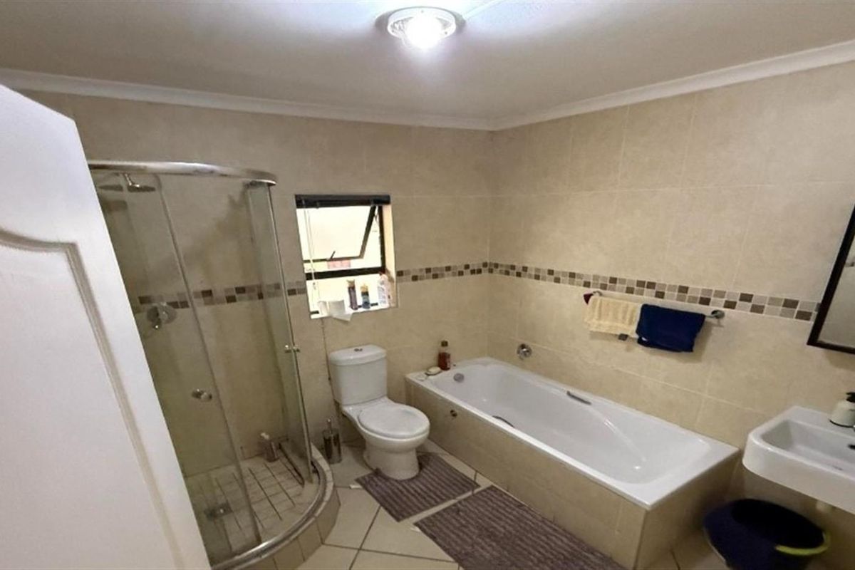 A functional bathroom featuring a glass-enclosed shower, a built-in bathtub, a wall-mounted basin, and neutral wall tiling with a decorative mosaic border.