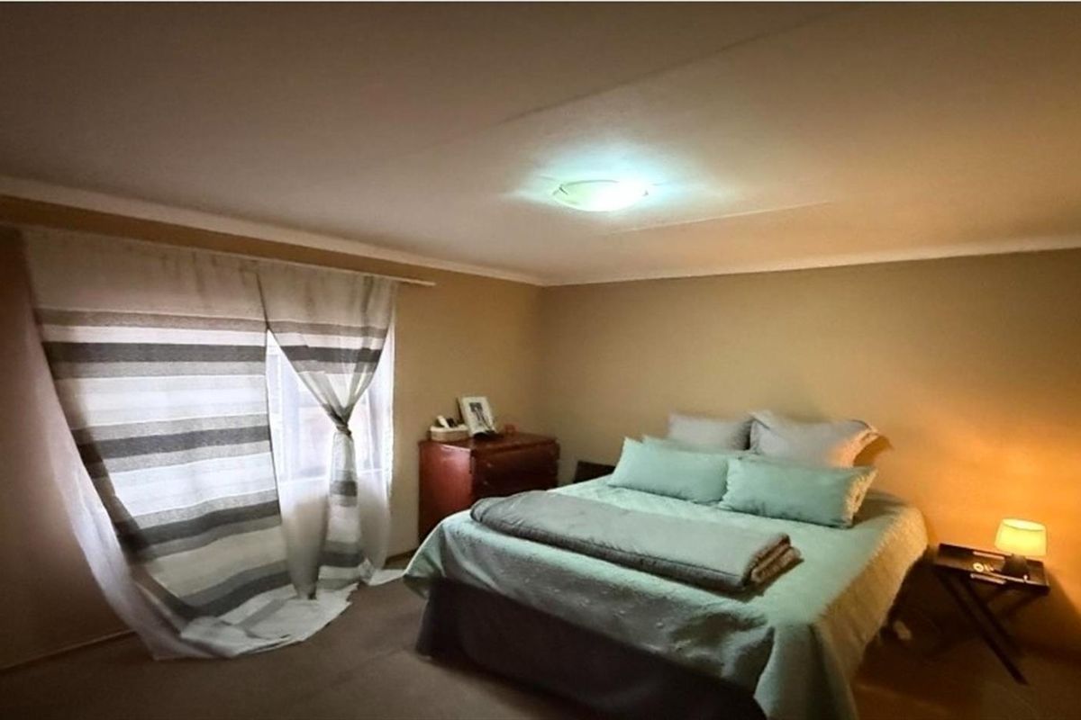 A standard bedroom featuring neutral wall tones, carpeted flooring, and a window with curtain fixtures.