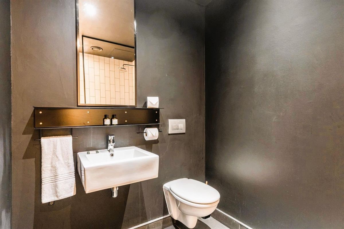 Modern bathroom featuring a wall-mounted basin, sleek dark wall finishes, and a concealed cistern toilet.