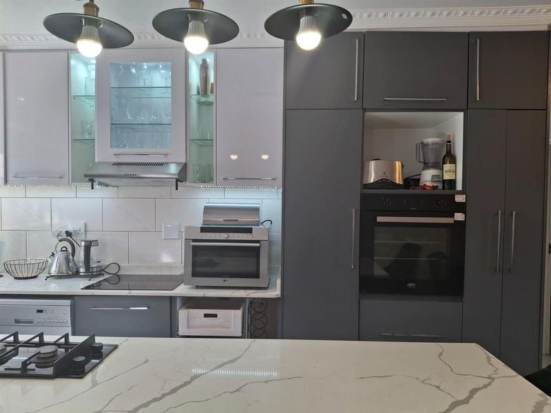 Modern kitchen featuring two-tone cabinetry, marble-look countertops, integrated oven, induction cooktop, and stylish pendant lighting.