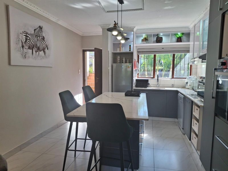 Modern kitchen featuring a central island with stone countertop, sleek cabinetry, tiled flooring, and integrated lighting, offering a functional and contemporary cooking space.