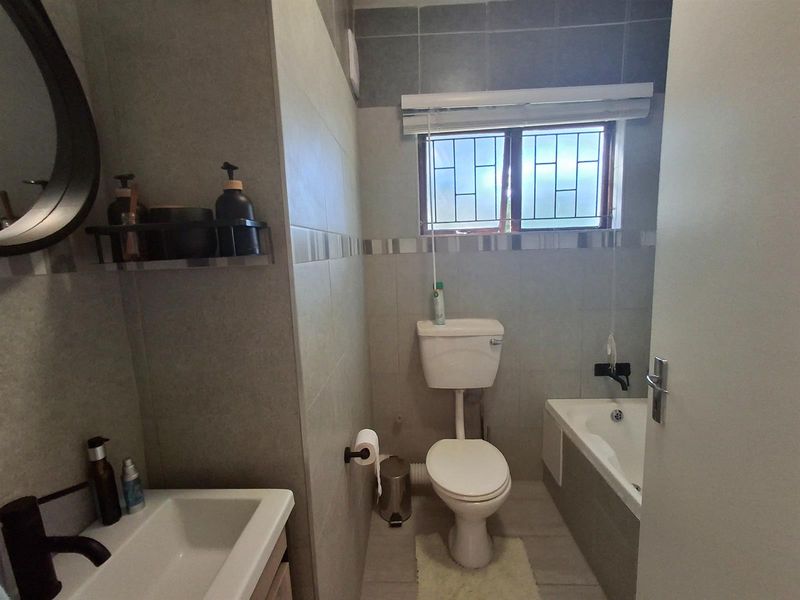 A modern bathroom featuring a built-in bathtub, a wall-mounted toilet, and a vanity basin with contemporary fixtures and neutral wall tiling.
