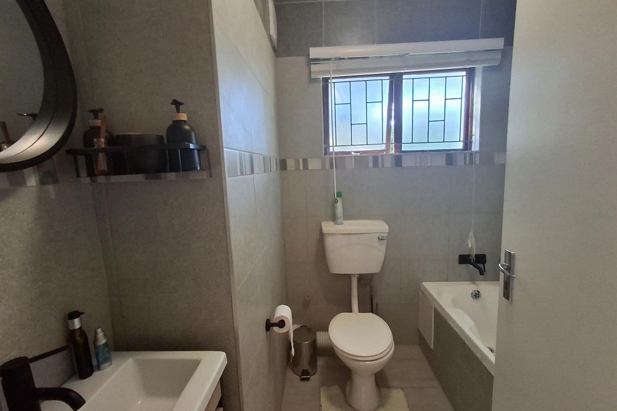 A modern bathroom featuring a built-in bathtub, a wall-mounted toilet, and a vanity basin with contemporary fixtures and neutral wall tiling.