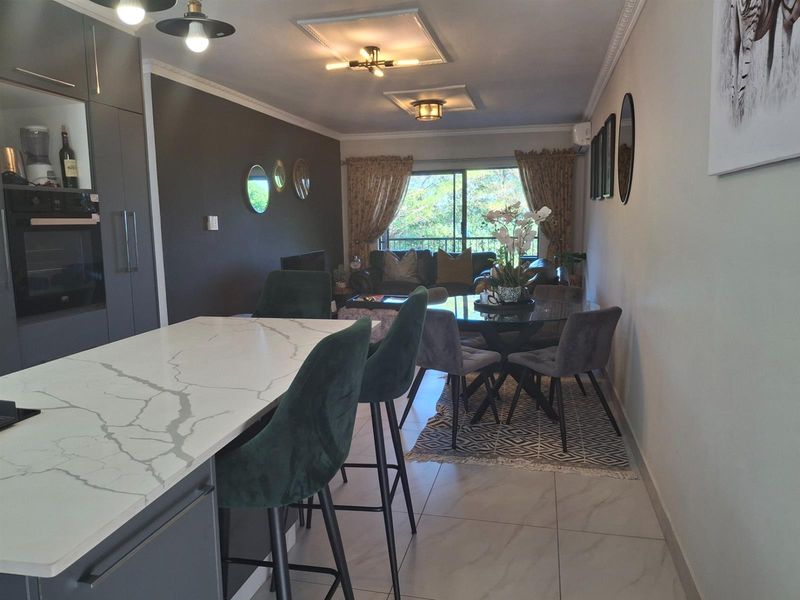 Open-plan living area featuring a modern kitchen with stone-topped island, integrated oven, and tiled flooring, flowing into a dining and lounge space.