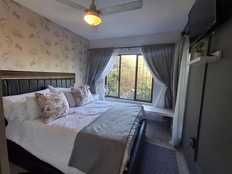 A cozy bedroom featuring a ceiling fan, tiled flooring, and a window with natural light, providing a comfortable and functional living space.