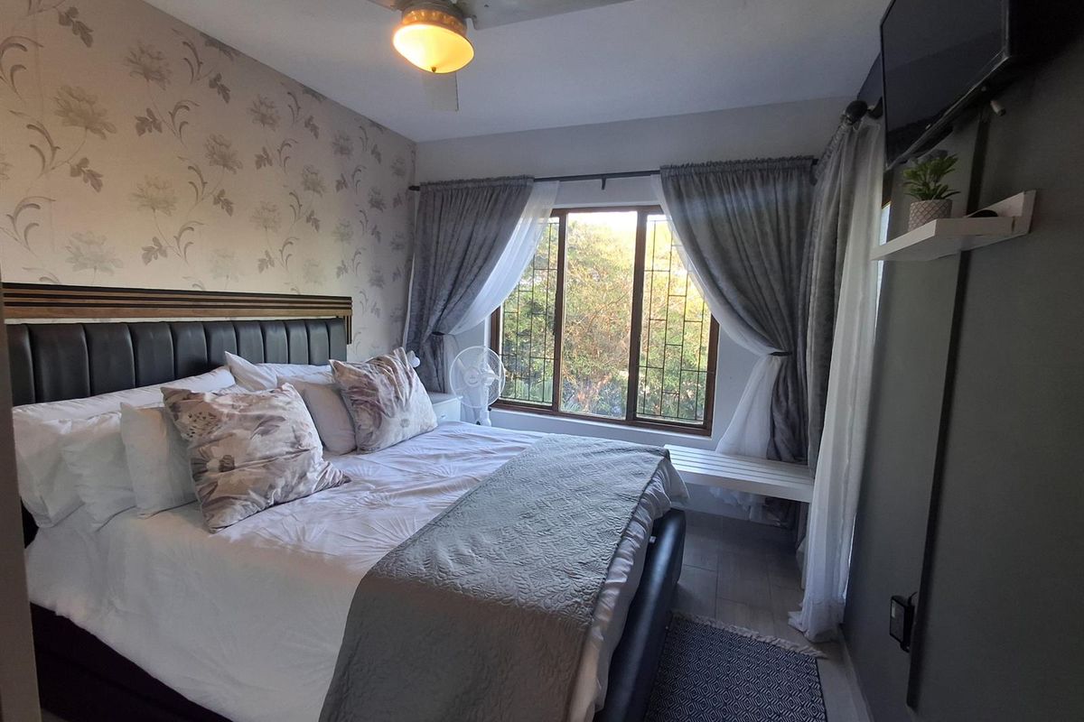 A cozy bedroom featuring a ceiling fan, tiled flooring, and a window with natural light, providing a comfortable and functional living space.