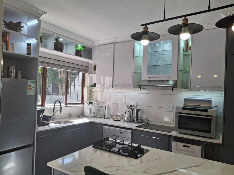 Modern kitchen featuring high-gloss cabinetry, stone countertops, a central island with a built-in gas hob, and integrated lighting.