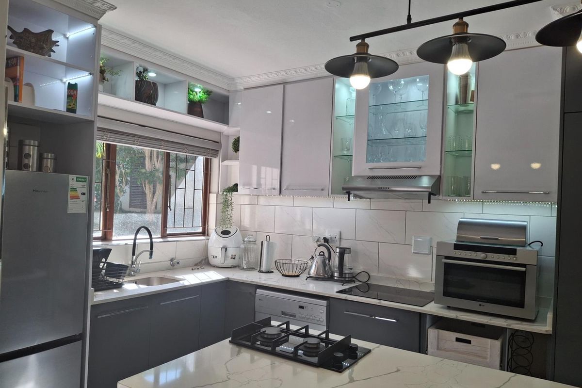 Modern kitchen featuring high-gloss cabinetry, stone countertops, a central island with a built-in gas hob, and integrated lighting.