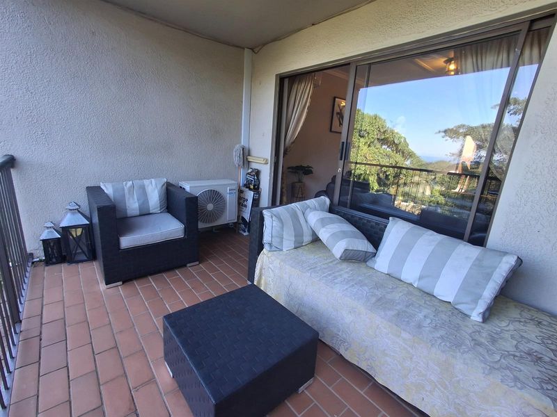 A covered balcony featuring terracotta tiled flooring, a metal balustrade, and a wall-mounted air conditioning unit, providing an outdoor extension to the living area.