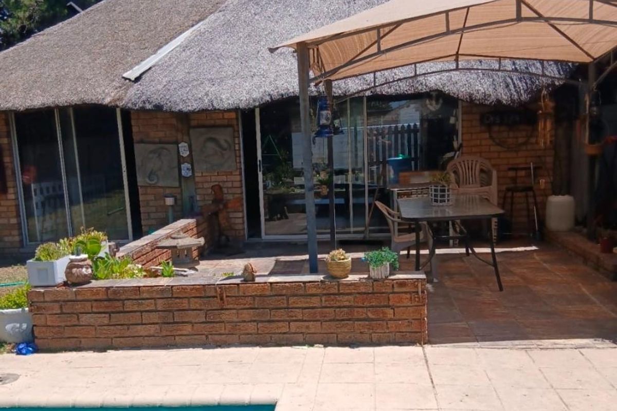 Rear exterior view featuring a thatched roof house, a paved patio area, and a swimming pool.