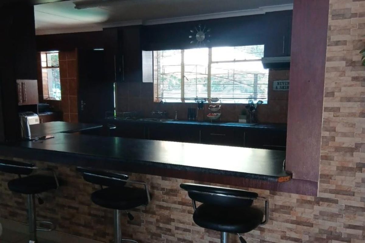 A kitchen featuring a breakfast bar counter with dark cabinetry, tiled splashbacks, and a window overlooking the exterior.