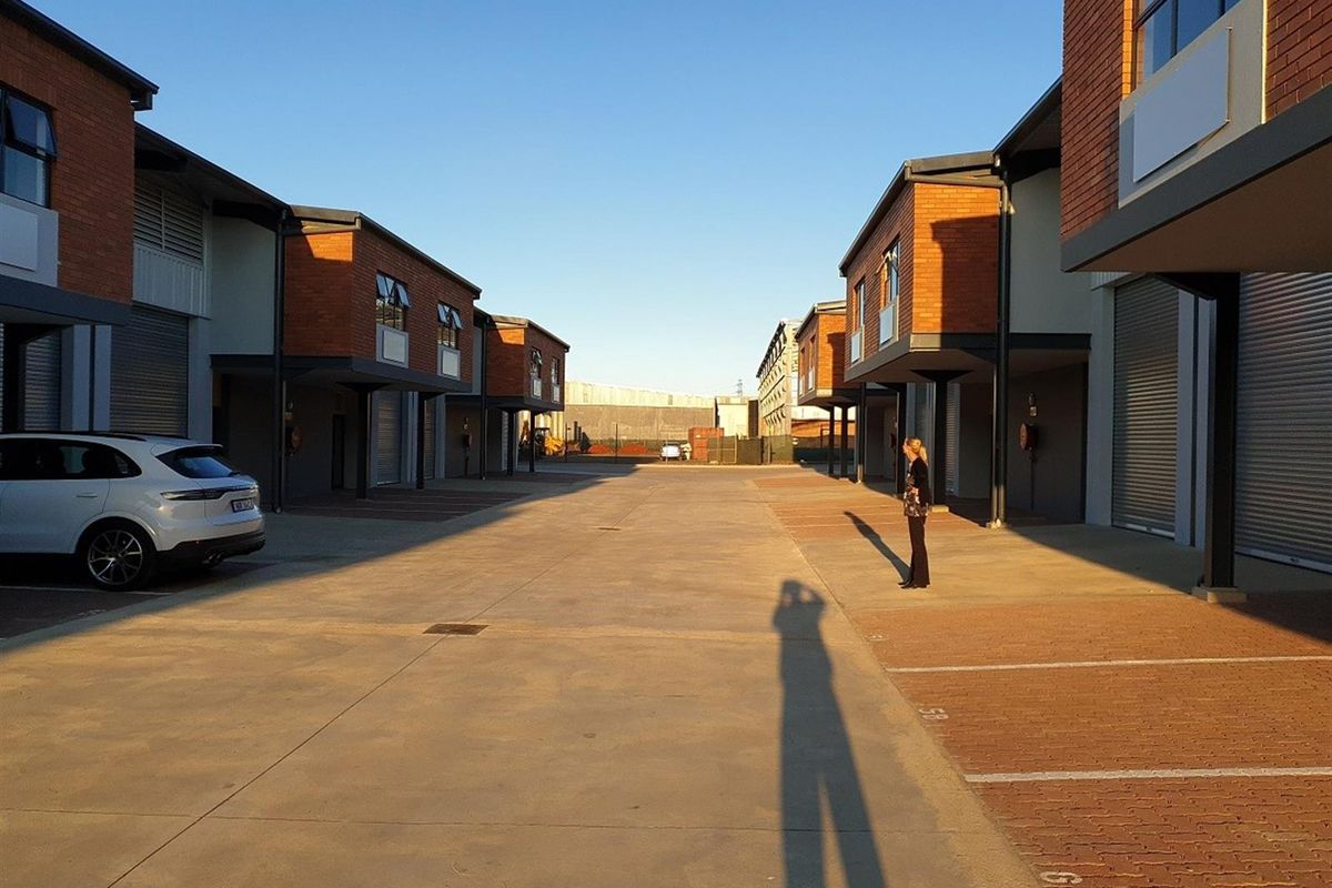 A view of an industrial complex featuring multiple units with brick facades, roller shutter doors, and paved driveway access.