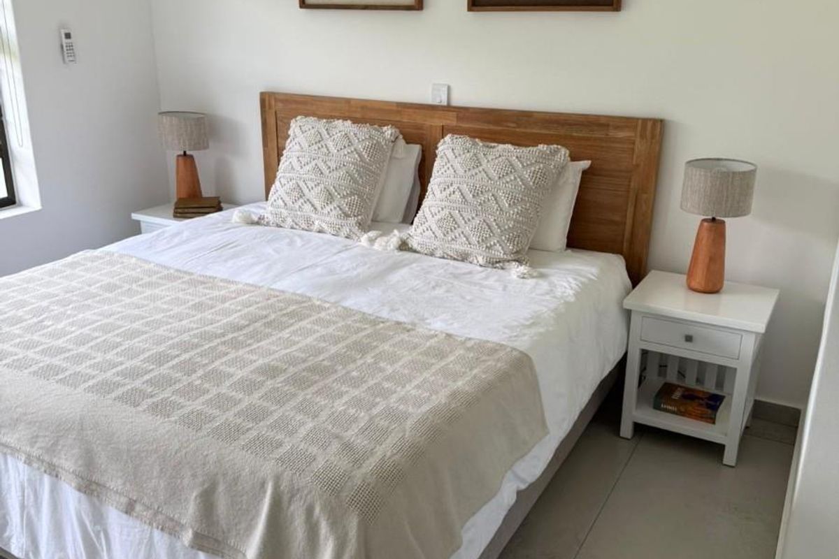 A well-maintained bedroom featuring neutral wall finishes, tiled flooring, and a built-in wooden headboard.