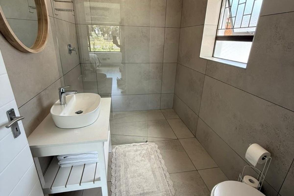 Modern bathroom featuring large format neutral floor-to-ceiling tiles, a glass-enclosed walk-in shower, and a contemporary vessel sink vanity.