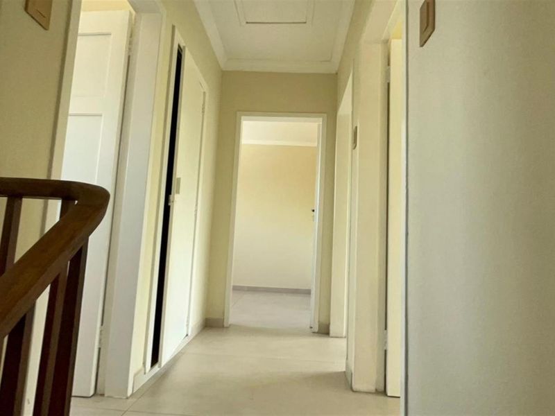 A clean, neutral-toned hallway featuring a wooden handrail and access to multiple rooms, providing a simple and functional transition space.