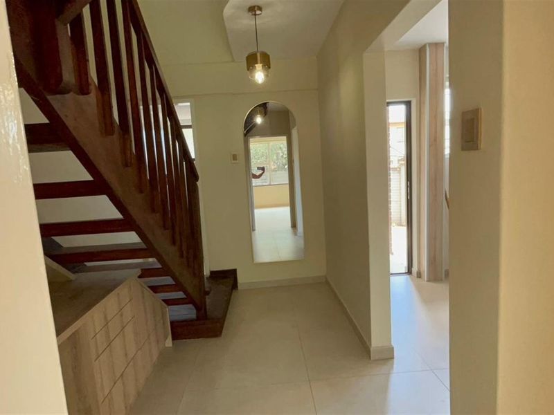A bright, tiled hallway featuring a wooden staircase with built-in storage underneath and an elegant arched transition to the adjacent living space.