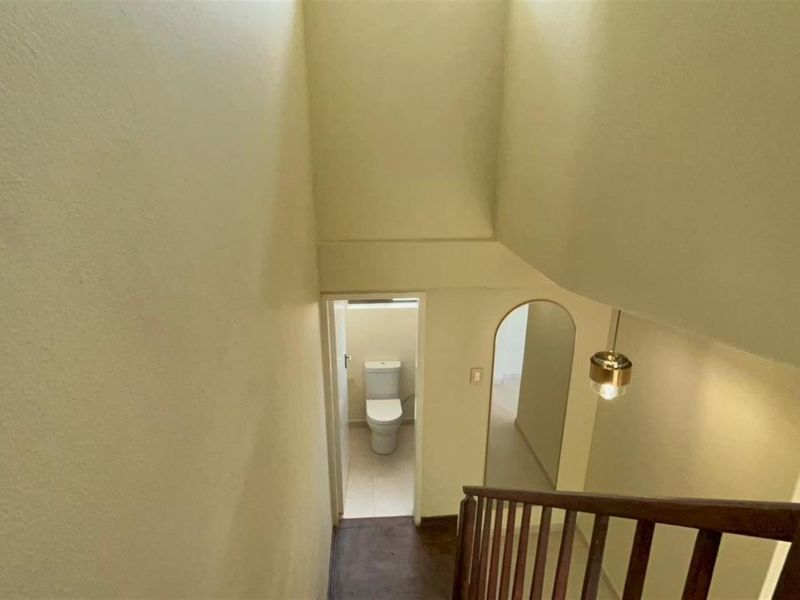 A view looking down a staircase towards a small bathroom, featuring a wooden balustrade and neutral wall finishes.