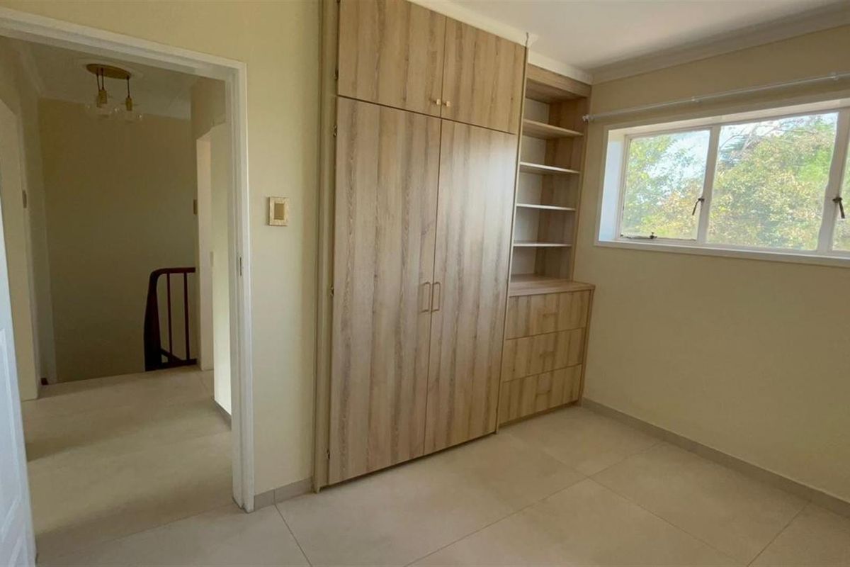 A bright, empty bedroom featuring modern light wood built-in cupboards with integrated shelving and neutral tiled flooring.