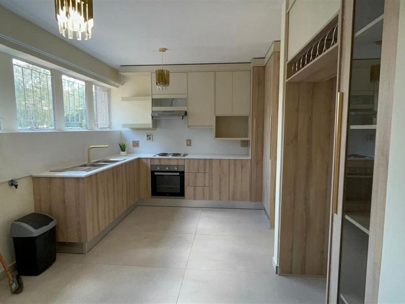 Modern, well-lit kitchen featuring light wood-finish cabinetry, stone countertops, integrated appliances, and large floor tiles, offering a clean and functional workspace.
