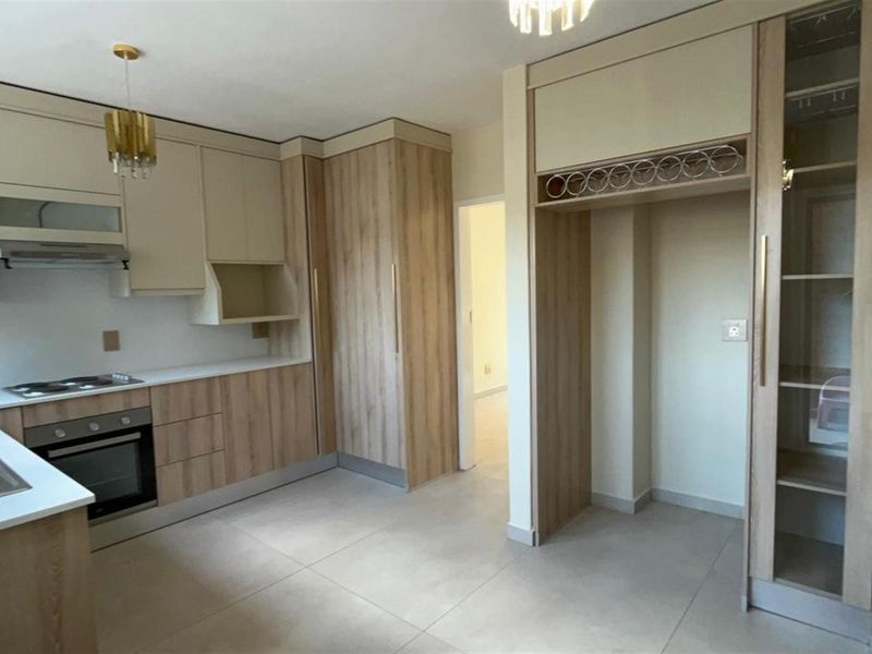 Modern kitchen featuring light wood-tone cabinetry, integrated oven, hob, extractor fan, and tiled flooring with a dedicated space for a refrigerator.