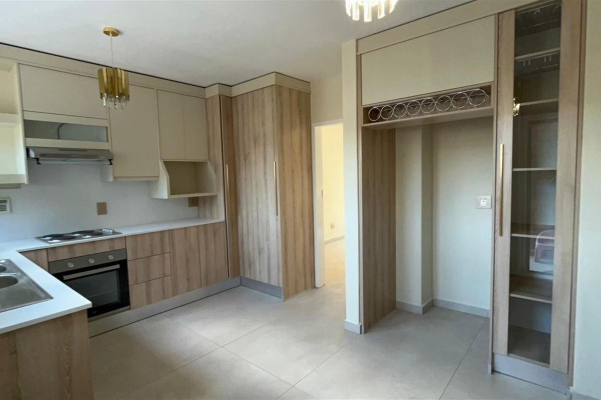 Modern kitchen featuring light wood-tone cabinetry, integrated oven, hob, extractor fan, and tiled flooring with a dedicated space for a refrigerator.