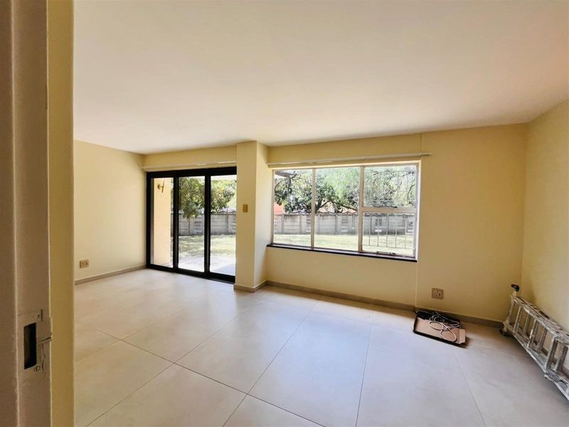 A bright, empty living room featuring large windows, tiled flooring, and a sliding glass door providing access to the rear garden area.