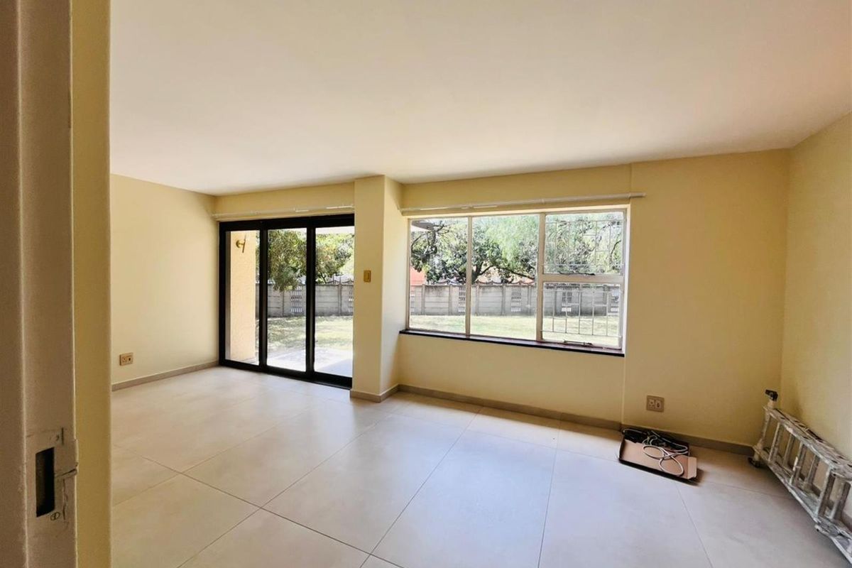 A bright, empty living room featuring large windows, tiled flooring, and a sliding glass door providing access to the rear garden area.