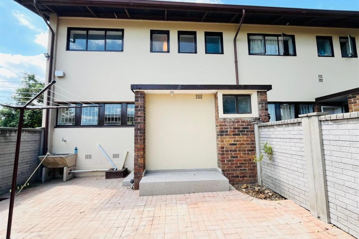 Rear exterior view of the townhouse featuring a paved courtyard, brick boundary wall, and a functional concrete wash trough area.